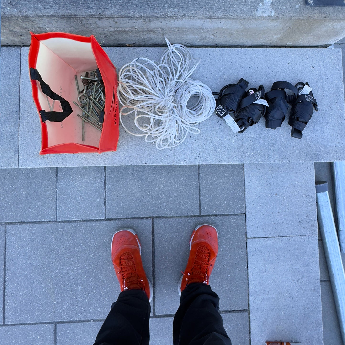 Red shoes on a tiled floor with a red bag, white rope, and black equipment nearby.